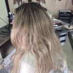 Păr blond cu rădăcini închise crescute și lungimi decolorate, cu aspect ușor tern și textură ondulată, înainte de vopsire într-un salon.